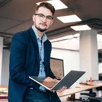 Man sitting on a desk holding a laptop